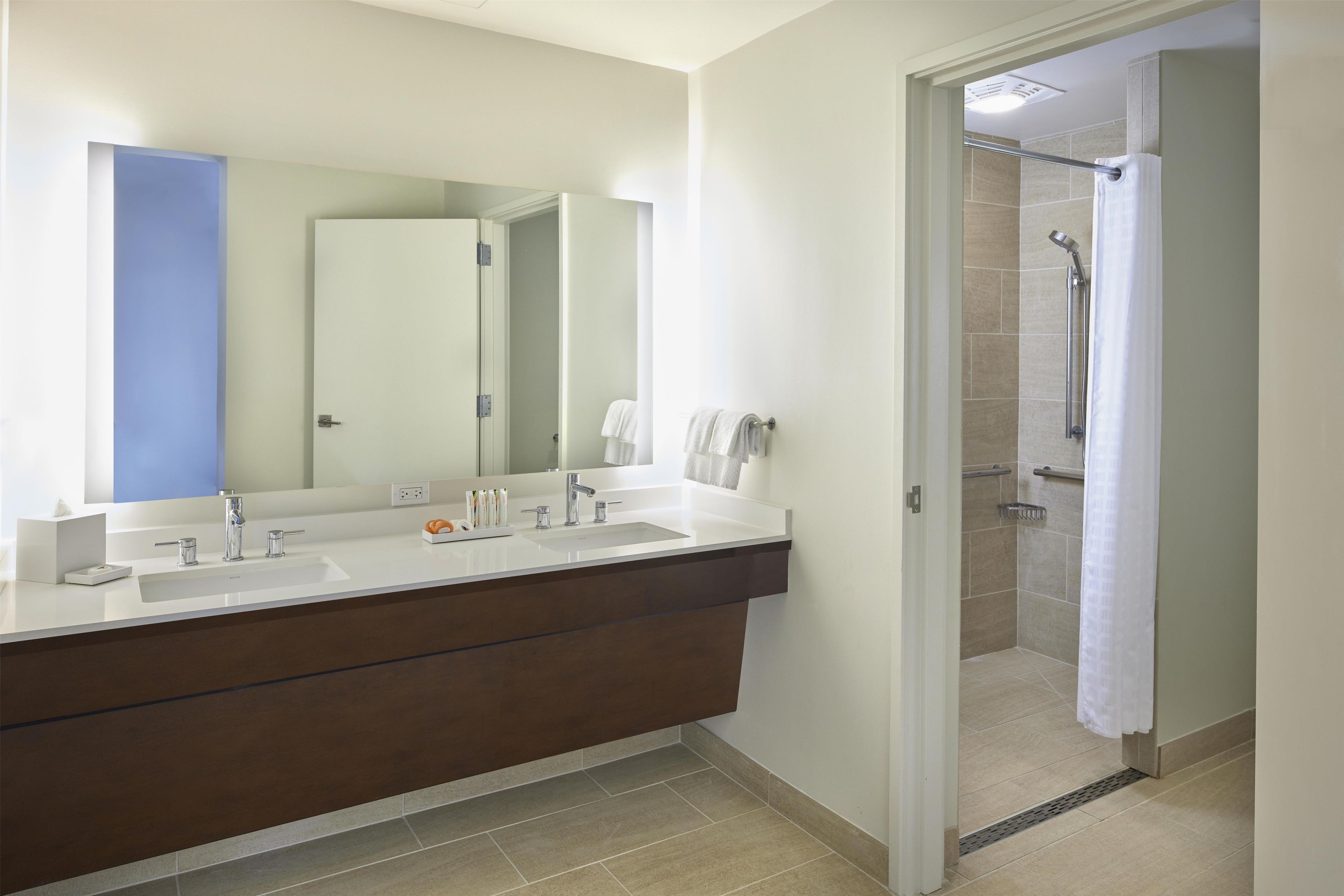 A modern bathroom with a double sink vanity, a large mirror, and a shower area.