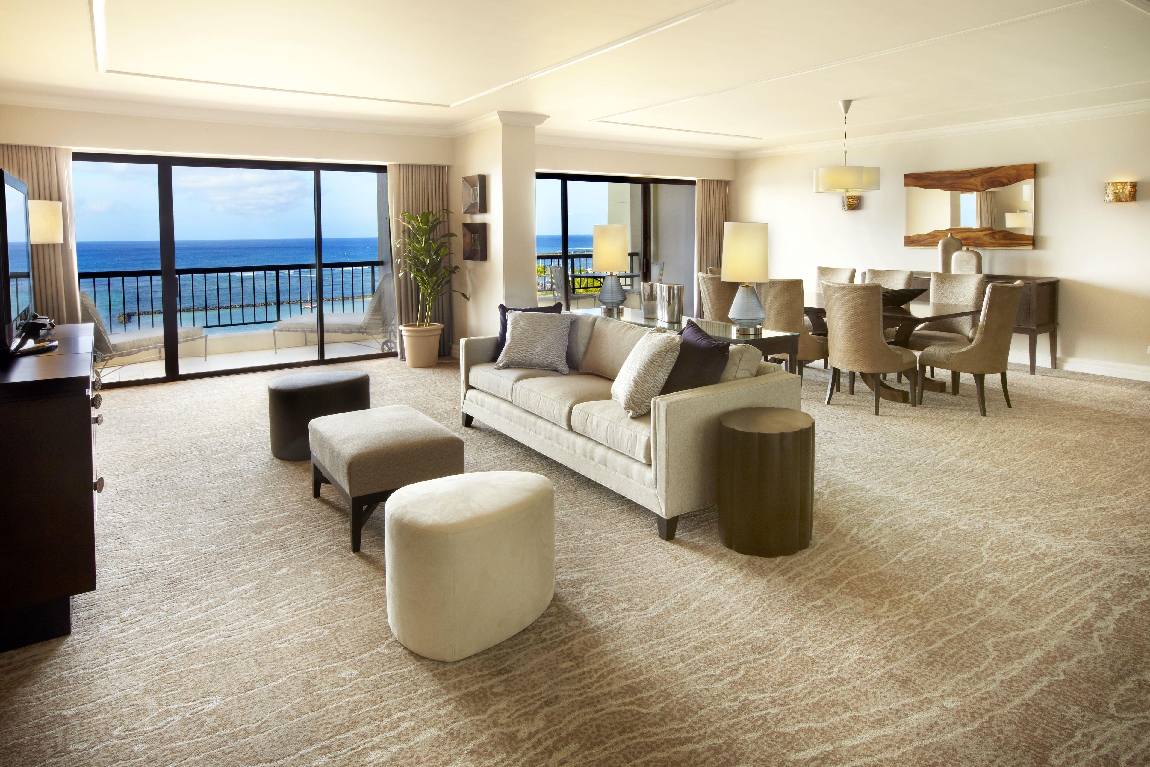Ein Hotelzimmer mit großem Balkon, einer Couch, einem Esstisch und einem Fernseher.