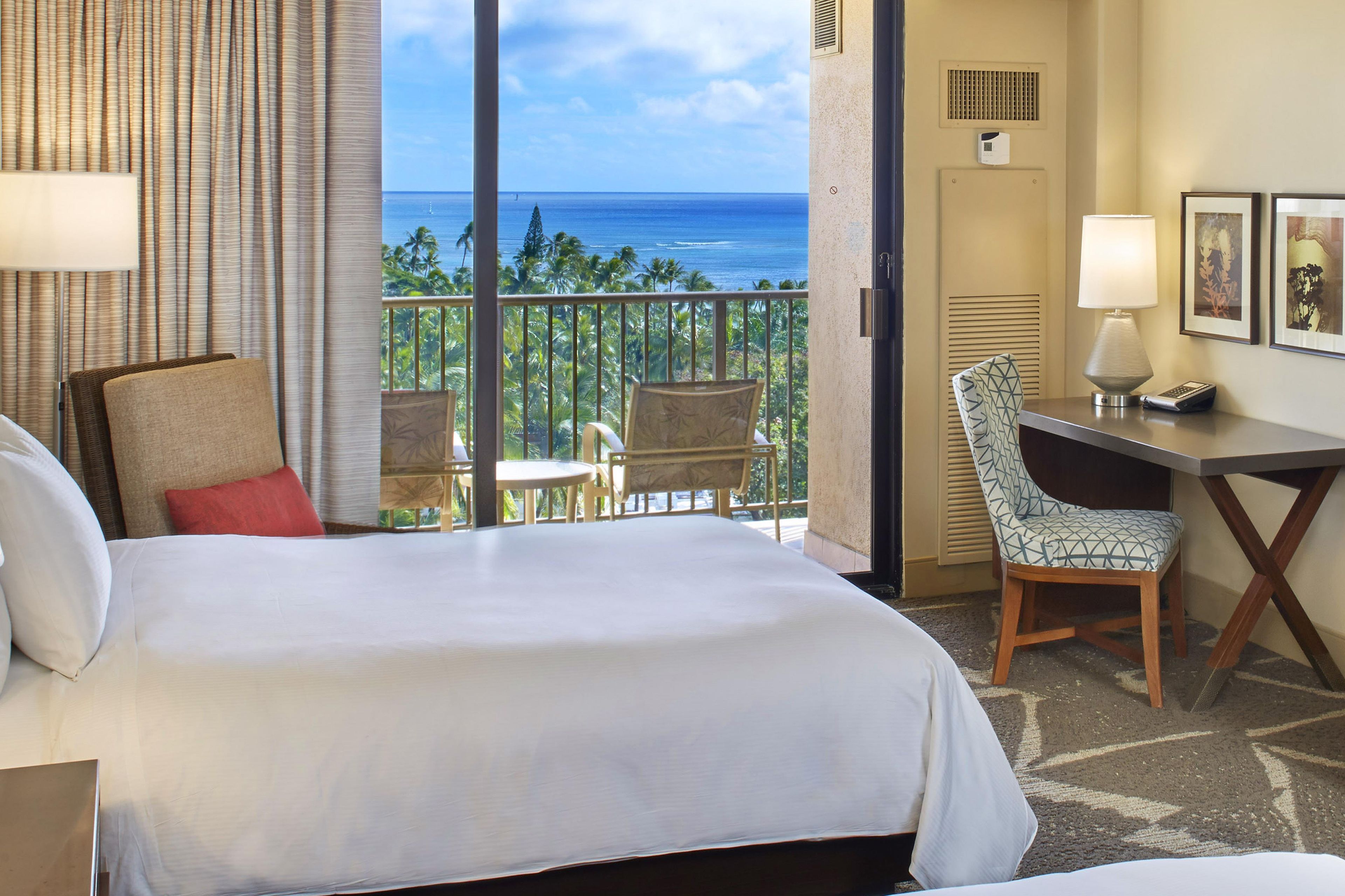 A hotel room with a bed, a desk, a chair, and a view of the ocean.
