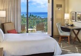 A hotel room with a bed, a desk, a chair, and a view of the ocean.