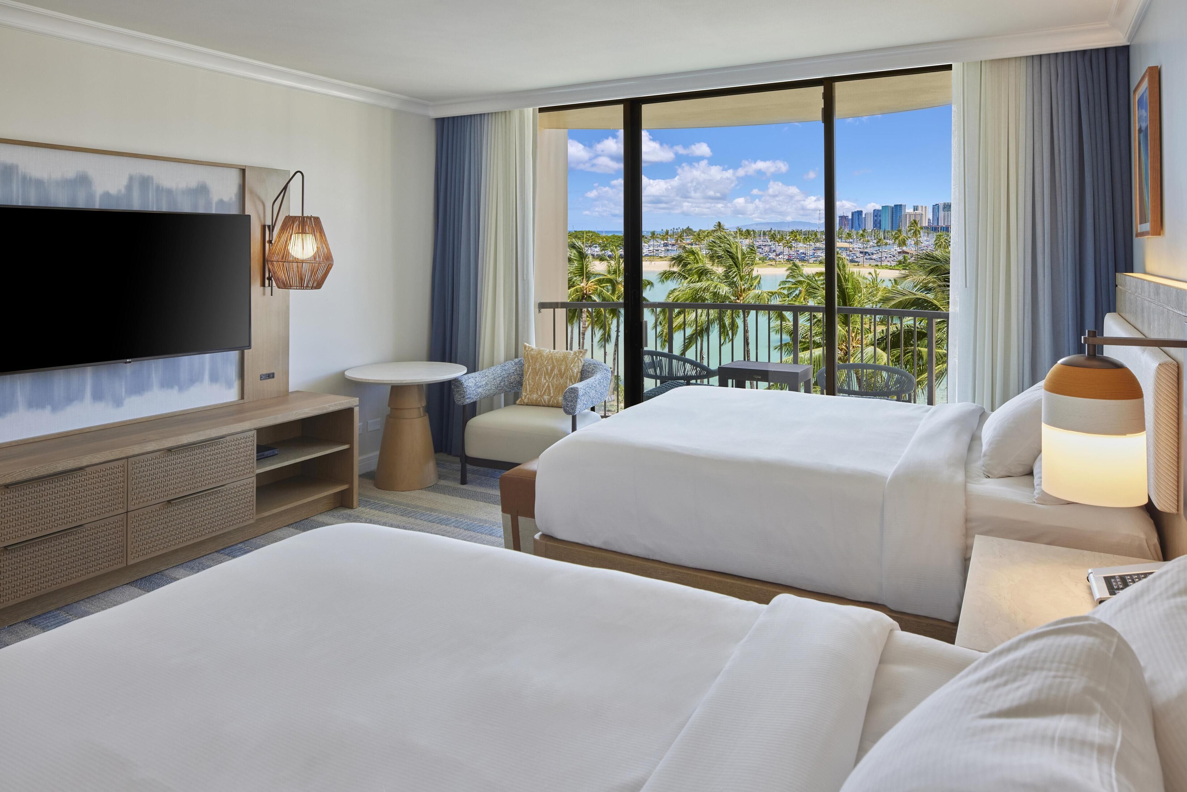 A hotel room with two beds, a TV, a small table, a chair, and a balcony with a city view.