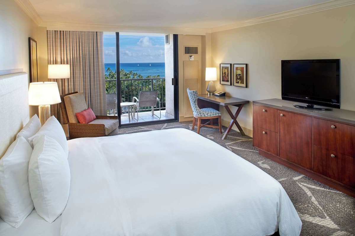 Habitación de hotel con una cama grande, televisión, escritorio y vista al océano.