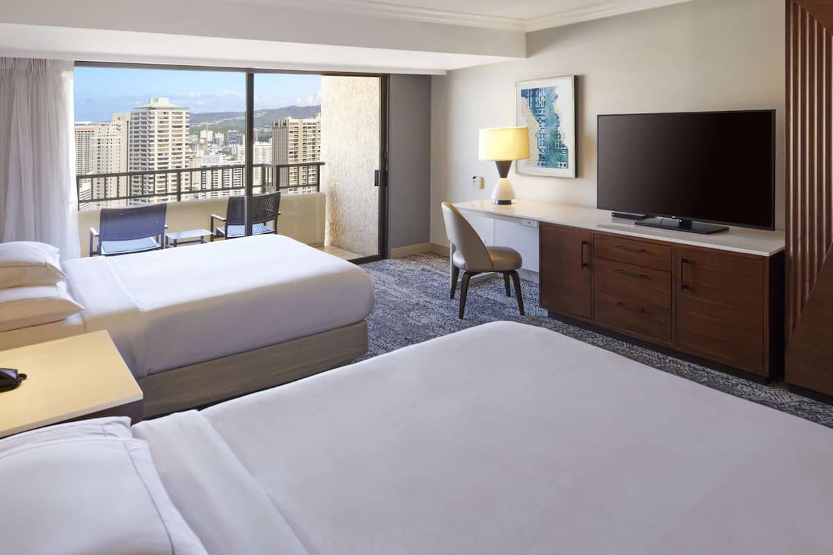 Habitación de hotel con dos camas, un escritorio, un televisor y vista a la ciudad.