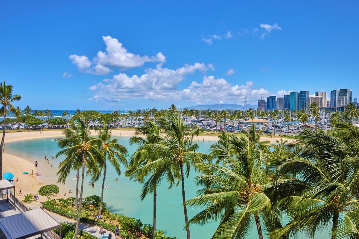 A beach with palm trees, a city skyline, and a clear blue sky.