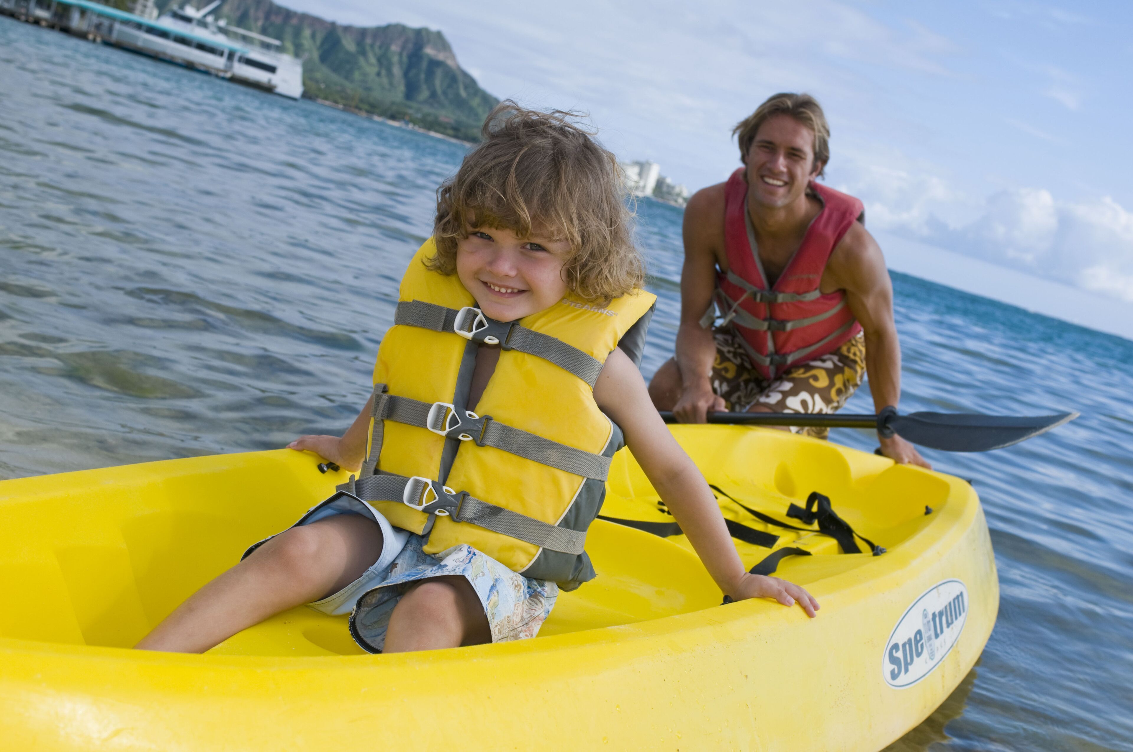 A person in a yellow inflatable raft on water with a mountainous background.