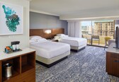 A hotel room with two beds, a coffee maker, a minibar, and a large window with a city view.