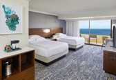 A hotel room with two beds, a desk, a coffee maker, and a view of the ocean.