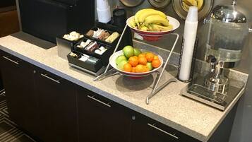A hotel breakfast bar with a fruit bowl, coffee dispensers, and a water dispenser.