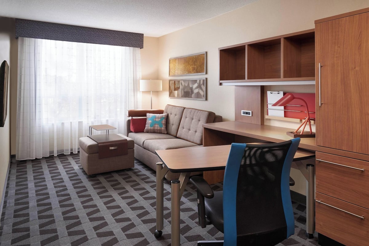 A hotel room with a sofa, a desk, a chair, a lamp, and a wardrobe.