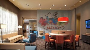 A hotel lobby with a cityscape mural, a round table with chairs, sofas, and a television on the wall.