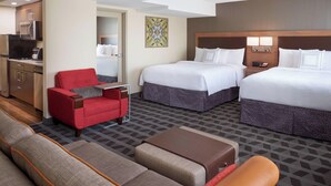 A hotel room with two beds, a red armchair, a sofa, a coffee table, and a TV.