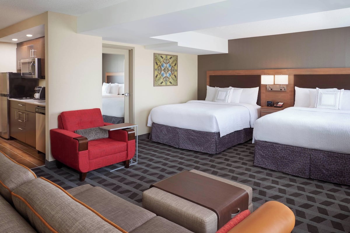 A hotel room with two beds, a red armchair, a sofa, a coffee table, and a TV.