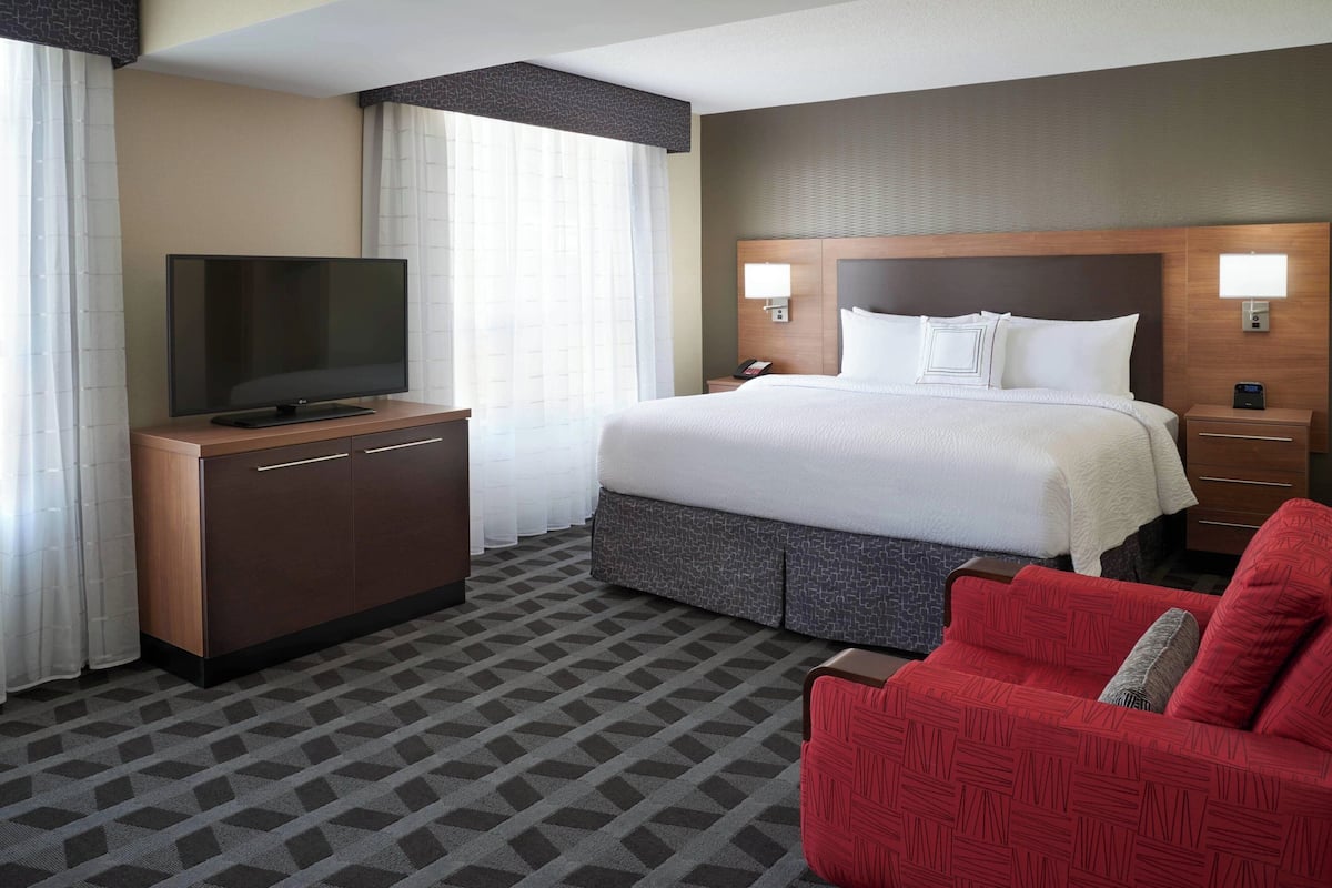 A hotel room with a large bed, a TV on a wooden cabinet, a red sofa, and a patterned carpet.