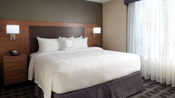 A hotel room with a large bed, two bedside lamps, a nightstand with a phone, and a window with sheer curtains.