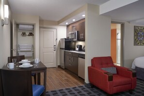 A compact hotel room with a kitchenette, a dining area, and a red armchair.