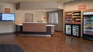 A hotel reception area with a wooden reception desk, a 'hello' sign, a digital screen displaying a map, and vending machines.