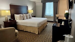 Una habitación de hotel con una cama grande, lámparas de noche, un escritorio, una silla y un televisor.
