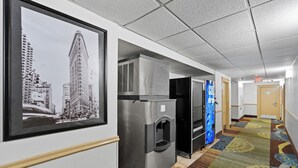 Un pasillo de hotel con una fotografía en blanco y negro de un paisaje urbano enmarcada, electrodomésticos de acero inoxidable y una alfombra colorida.