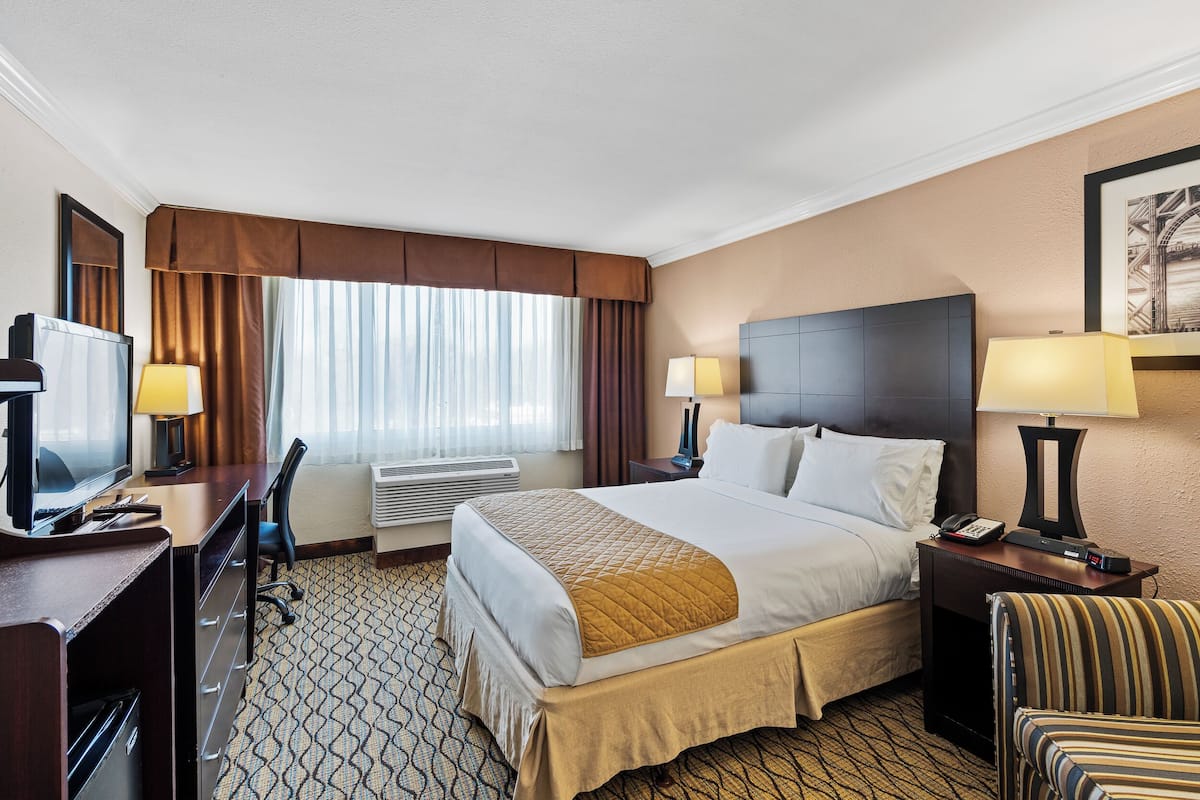 Habitación de hotel con una cama, lámparas de noche, un escritorio con ordenador, televisión y una silla.