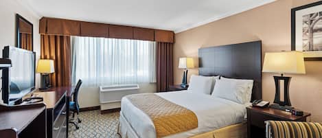 Een hotelkamer met een bed, bedlampen, een bureau met een computer, een televisie en een stoel.