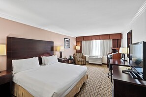 Enjoy a restful stay in this cozy room featuring a large bed, desk with flat-screen TV, and comfortable armchair.