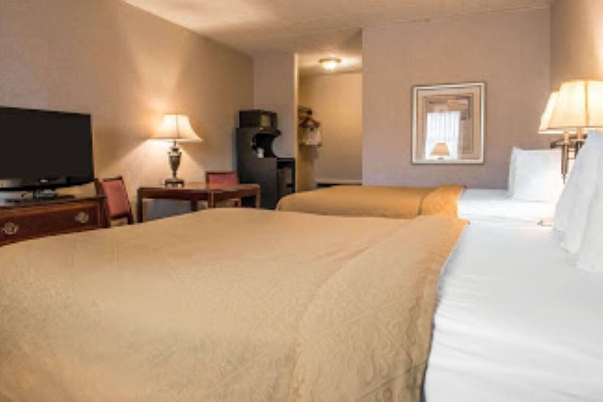 A hotel room with a large bed, a television, a desk with a lamp, and a mirror on the wall.