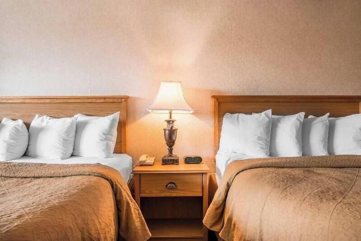A hotel room with two beds, a nightstand with a lamp, a phone, and a small drawer.