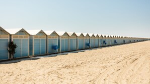 Una hilera de cabañas de playa frente a una playa arenosa.