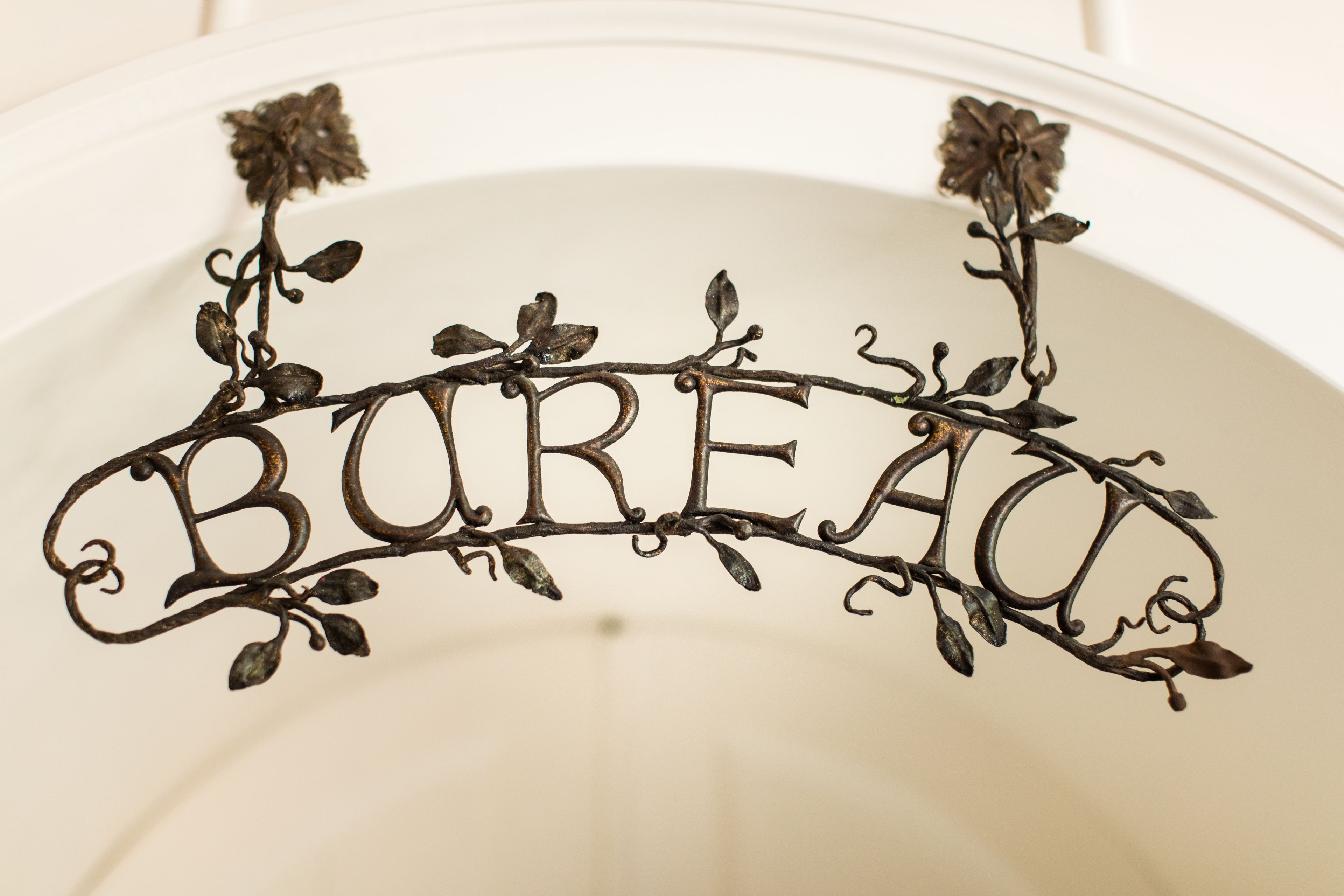 Uma placa de metal decorativa com a palavra "BUREAU" rodeada por folhagem.