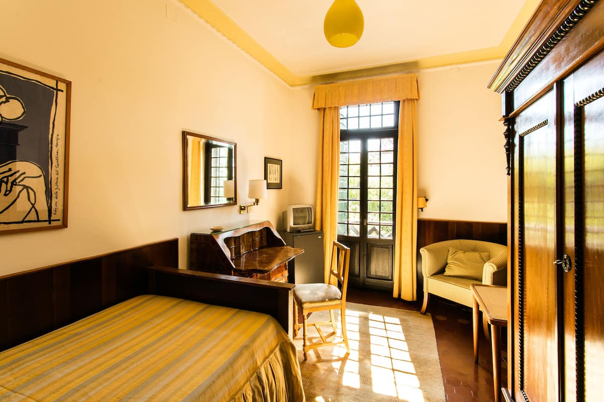 A hotel room with a bed, a desk with a chair, a television, and a wardrobe.