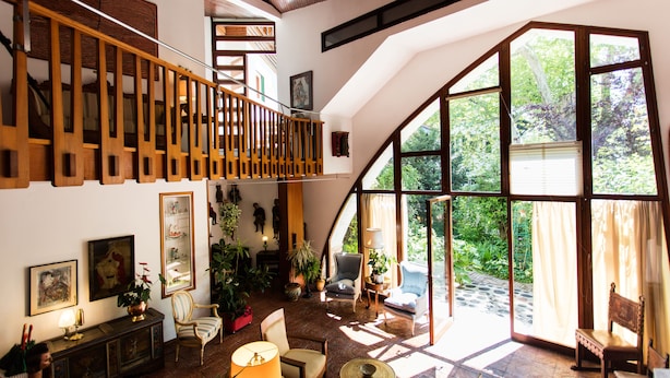 Amplia sala de estar con techo alto, escalera de madera y grandes ventanales con vistas al exterior.