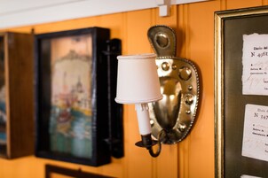 A wall-mounted lamp with a white shade, a framed painting, and a wall with two documents.