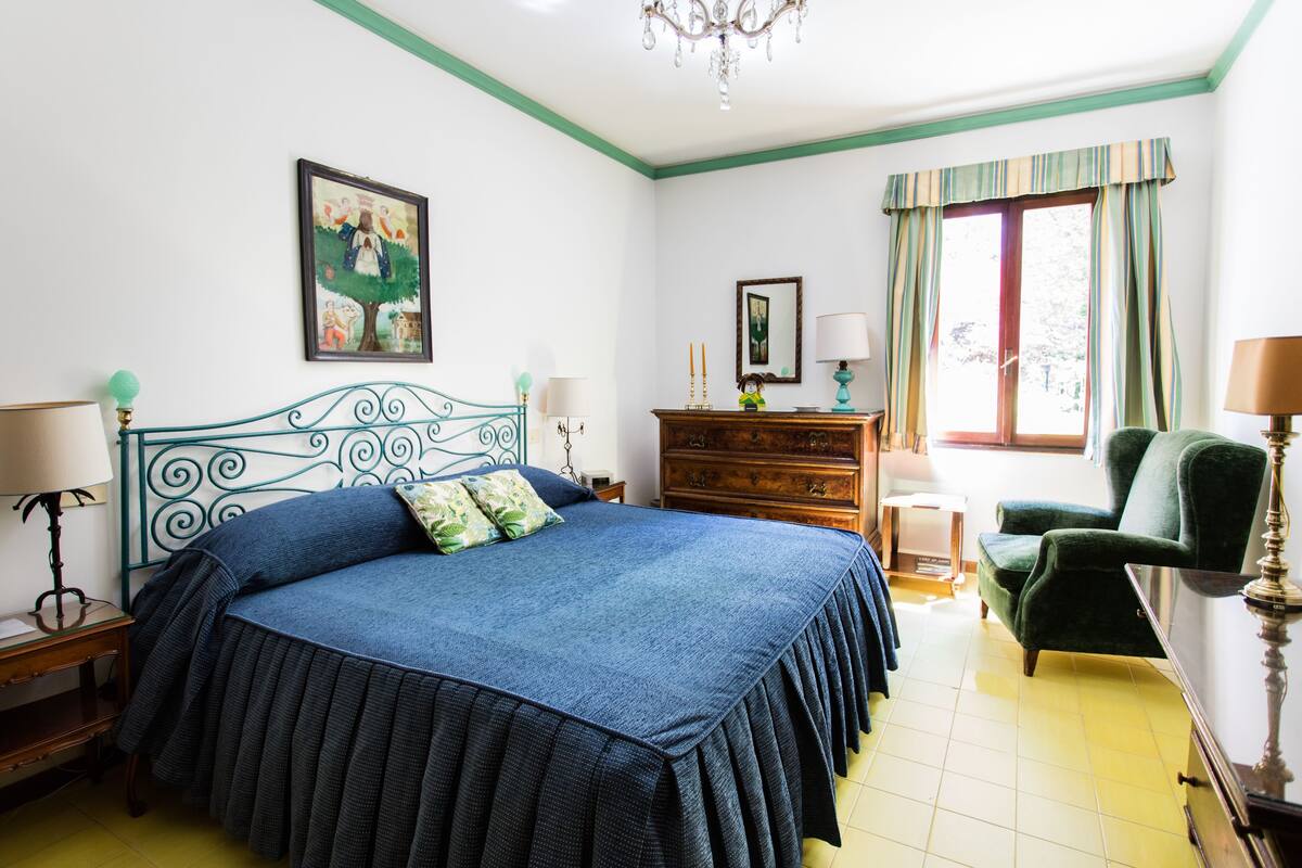 A bedroom with a bed, dresser, chair, and a painting on the wall.
