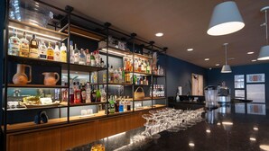 Zona de bar con estantes llenos de botellas de licores, una barra con vasos e iluminación colgante.