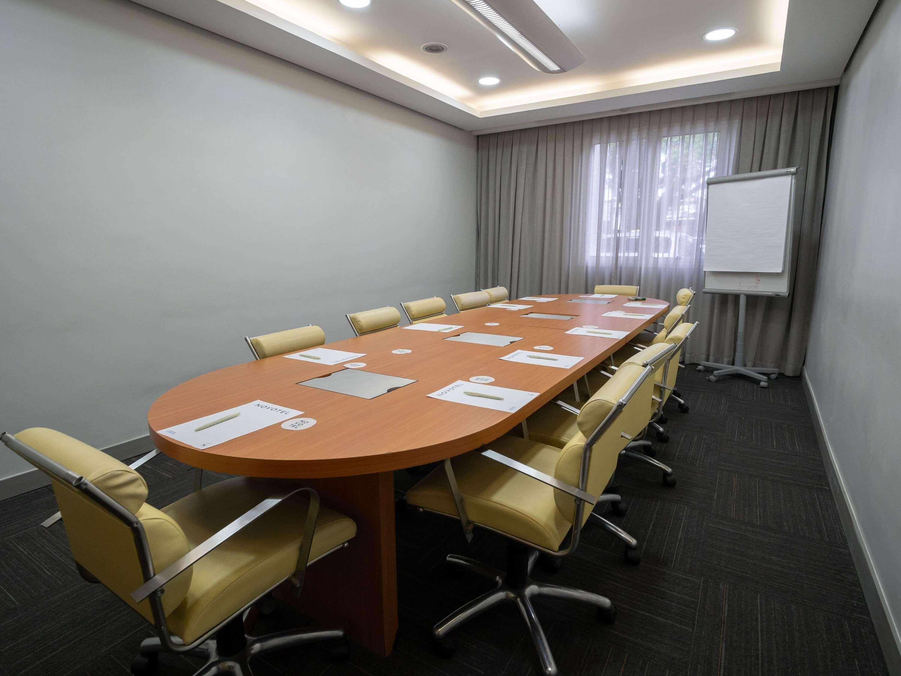 Un salón de conferencias con una larga mesa, sillas, una pizarra y una pantalla para proyector.