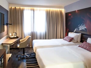 Habitación de hotel con dos camas, un escritorio con silla, cafetera y un ventanal con cortinas.