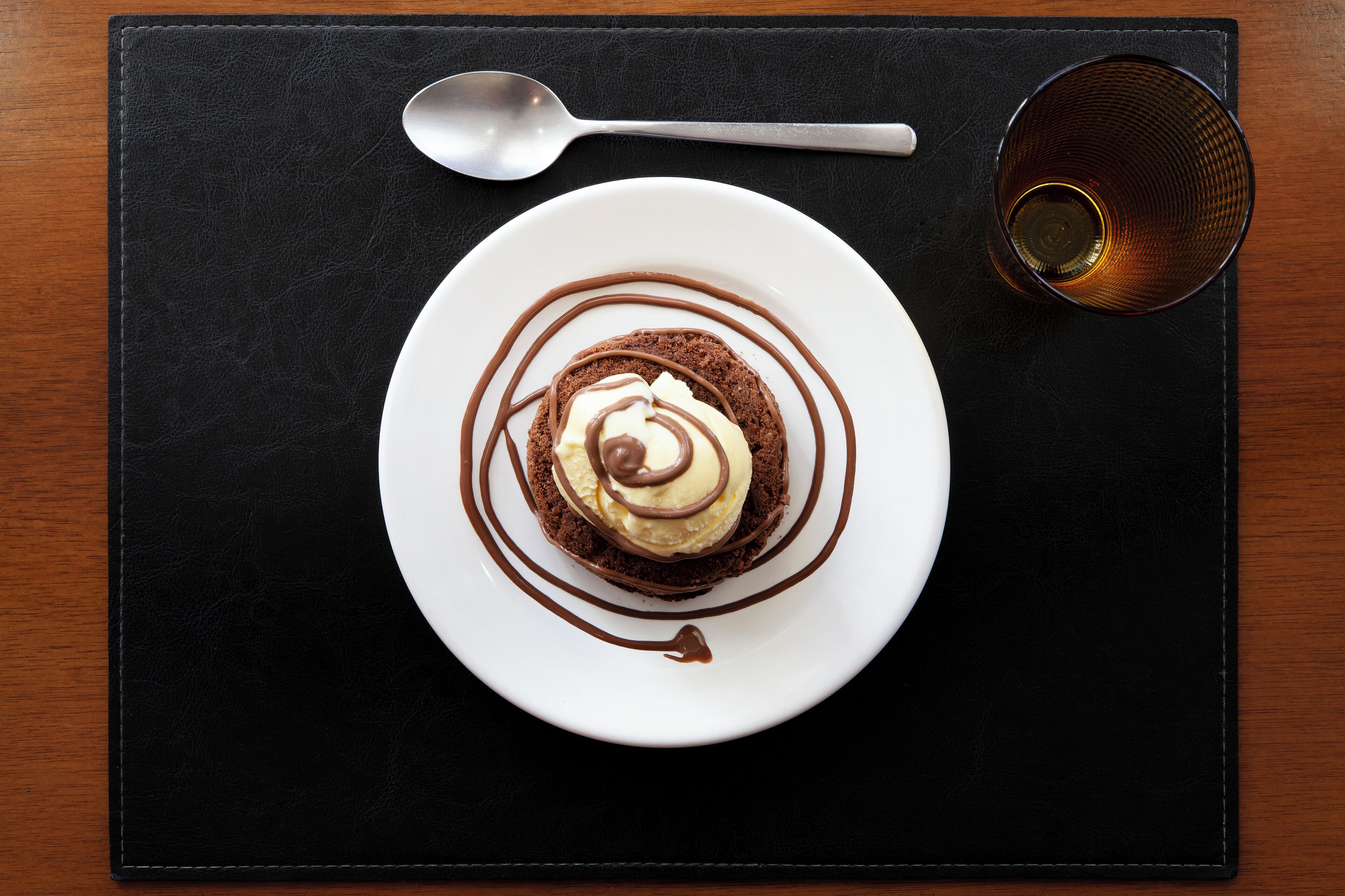 A dessert on a white plate with chocolate sauce and a spoon on a black table.