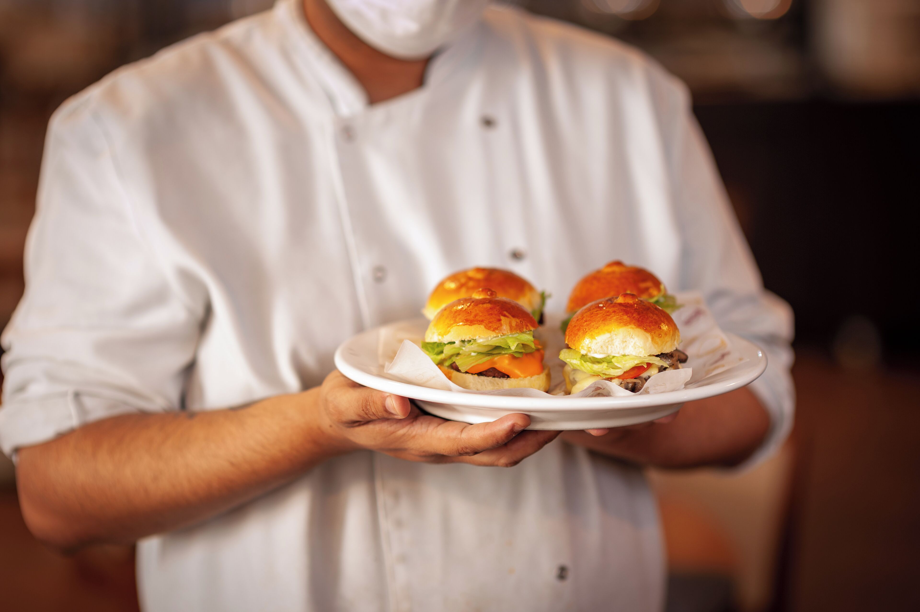 A person holding a plate with four burgers.