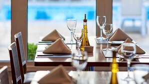 Mesa de comedor dispuesta con servilletas, copas de vino y una botella, con vista a una piscina.
