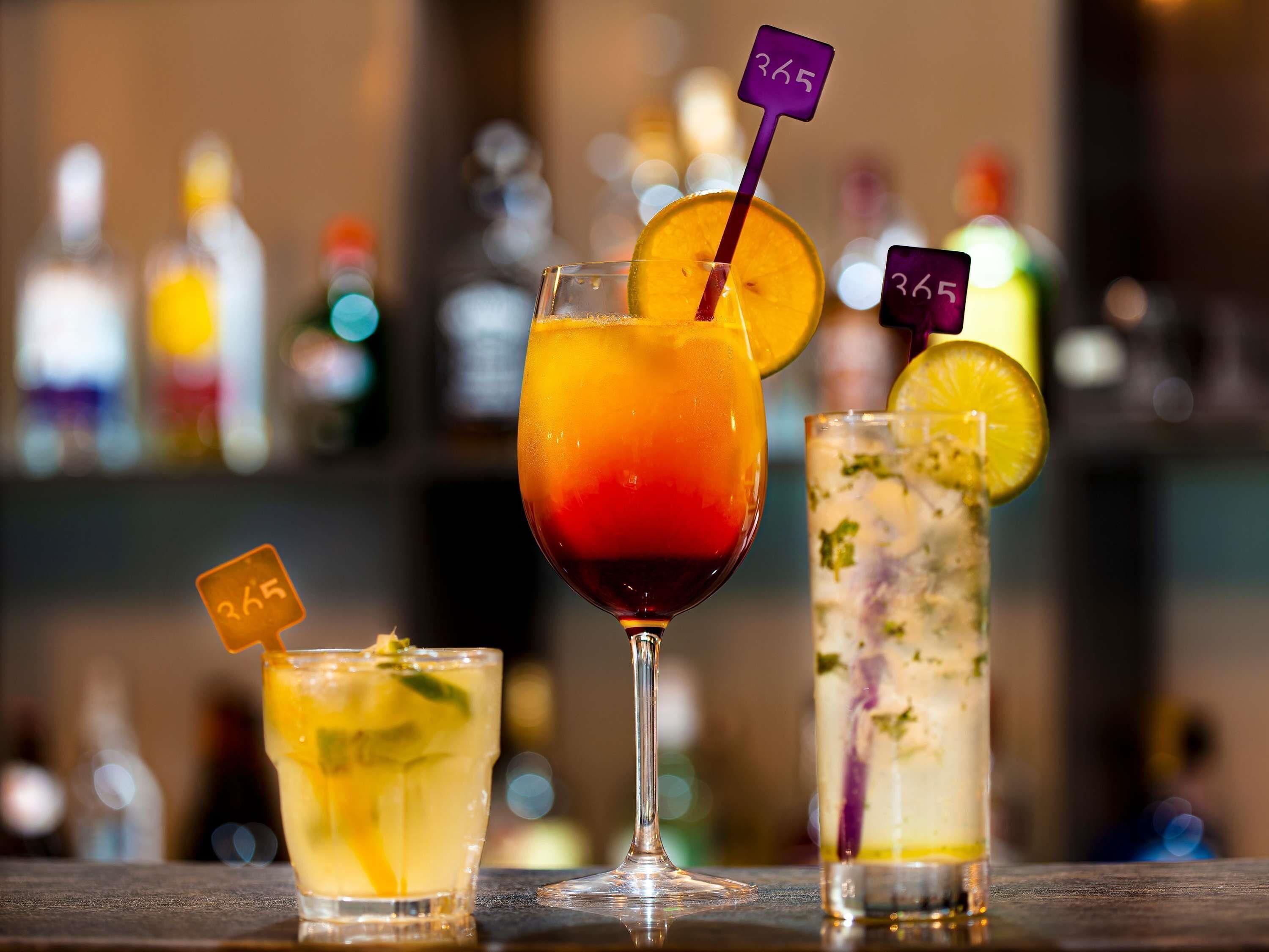 Three cocktails on a bar counter with a blurred background of bottles.