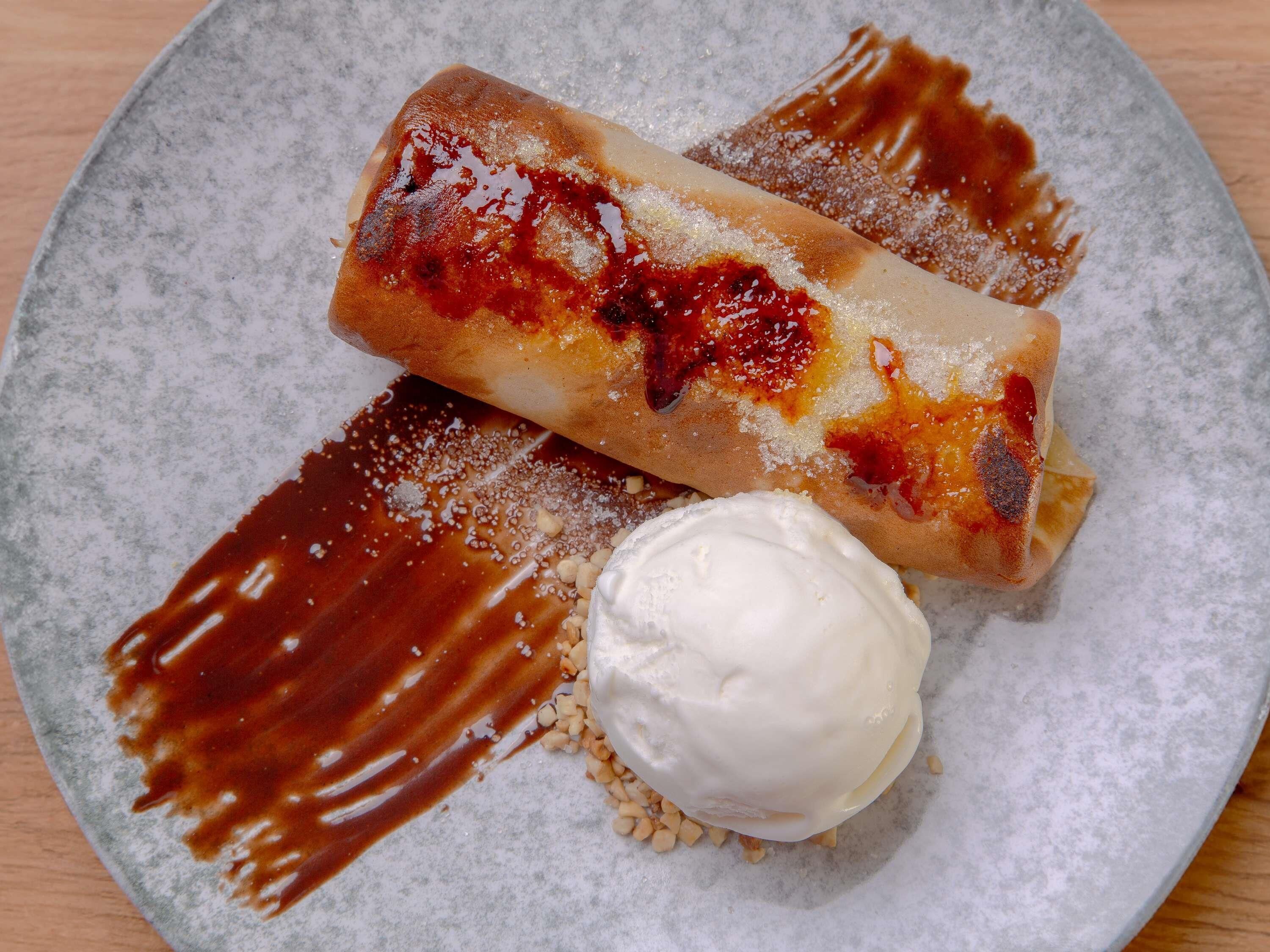 A dessert plate with a rolled pastry, a scoop of ice cream, and a drizzle of sauce.