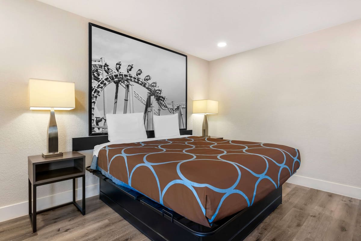 Una cama bien hecha con una colcha estampada, dos mesitas de noche con lámparas, un cuadro en la pared y suelo de madera.