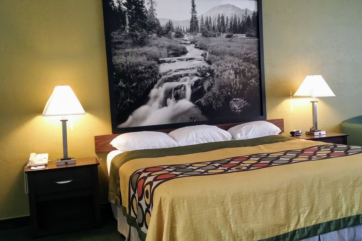 A hotel room with a bed, two bedside lamps, a telephone, a framed picture of a waterfall, and a blue chair.