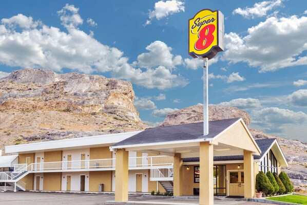 Um motel com uma placa chamativa 'Super 8', um edifício de dois andares com varanda e um cenário montanhoso.