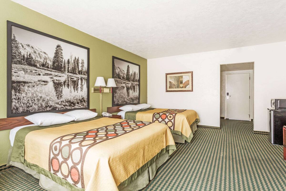 A hotel room with two beds, a desk, a lamp, and a television.