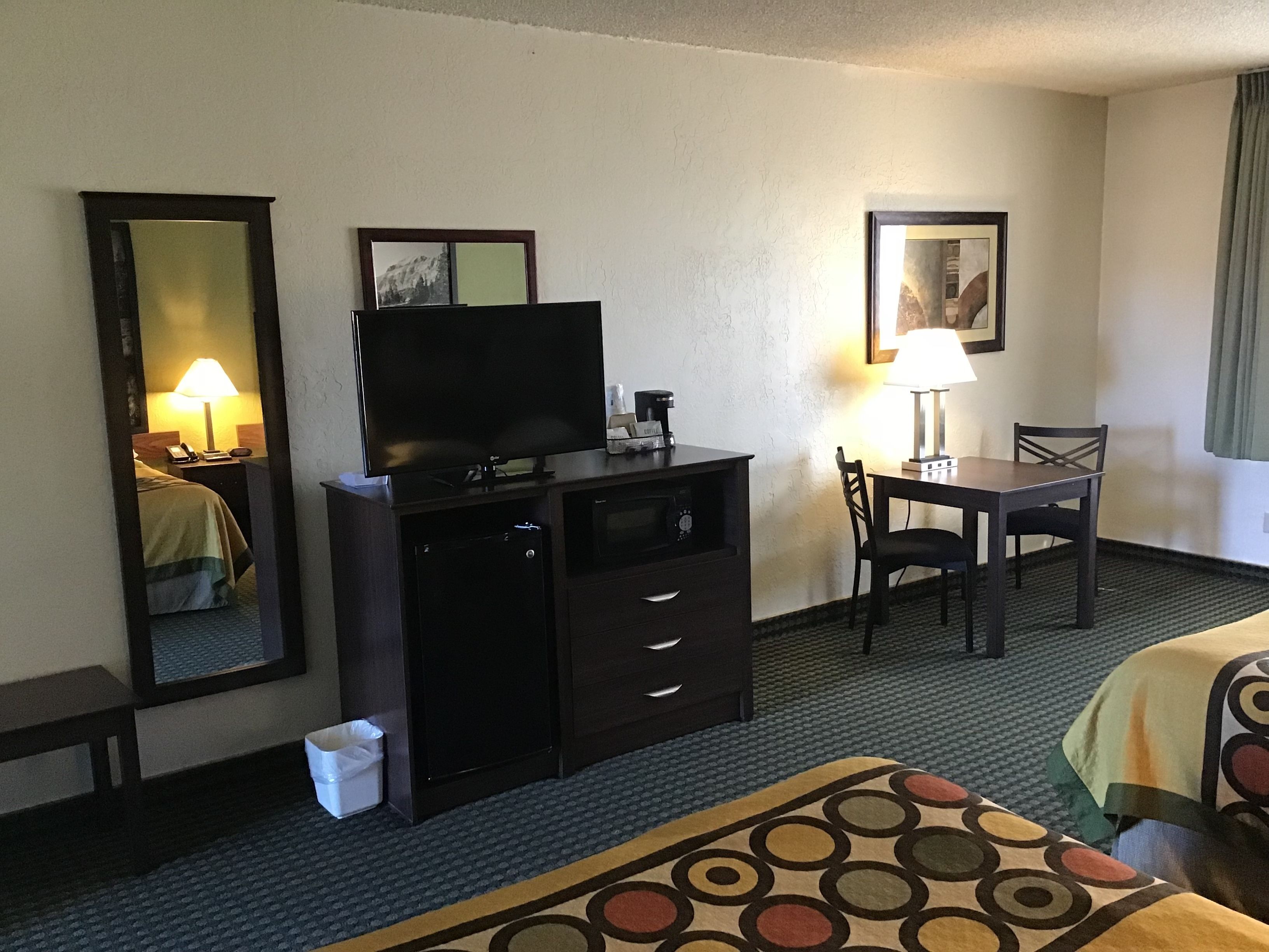 Habitación de hotel con cama, televisor en una cómoda, escritorio con silla y lámpara.