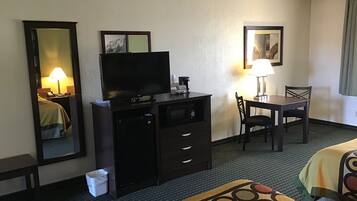 Habitación de hotel con cama, televisor en una cómoda, escritorio con silla y lámpara.