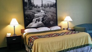 A hotel room with a bed, two bedside lamps, a telephone, a framed picture of a waterfall, and a blue chair. - Super 8 by Wyndham Wendover (Wendover)