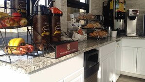 A kitchen counter with coffee dispensers, a bread display, and a fruit basket. - Super 8 by Wyndham Wendover (Wendover)
