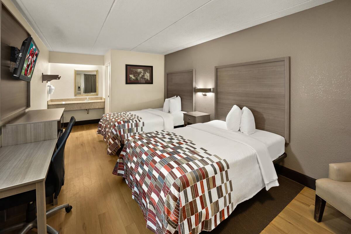 A hotel room with two beds, a desk, a chair, a TV, and a bathroom mirror.